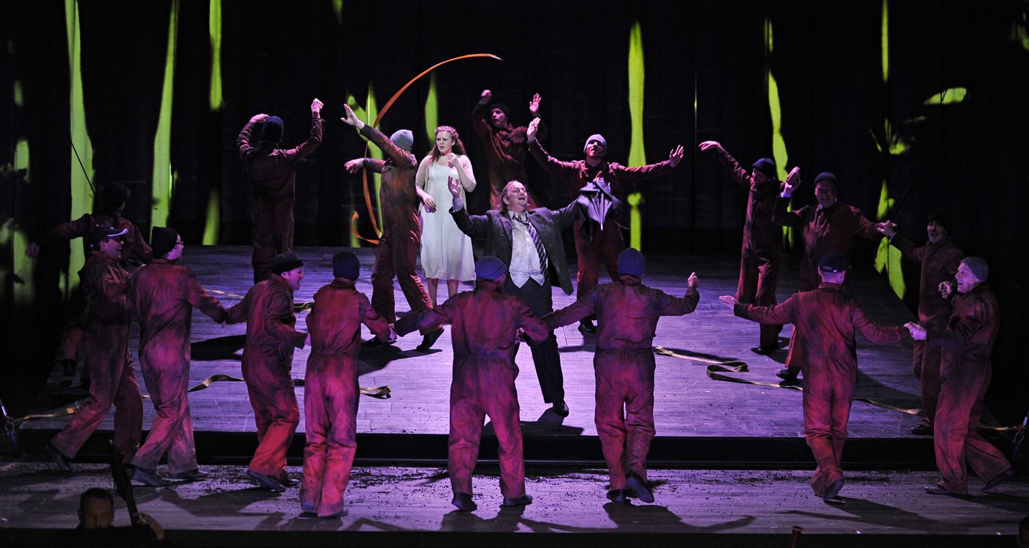 Man and woman surrounded by group in orange jumpsuits in ENO's The Magic Flute