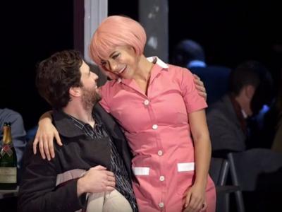 actor and actress in pink wig smile at each other on stage of La Boheme