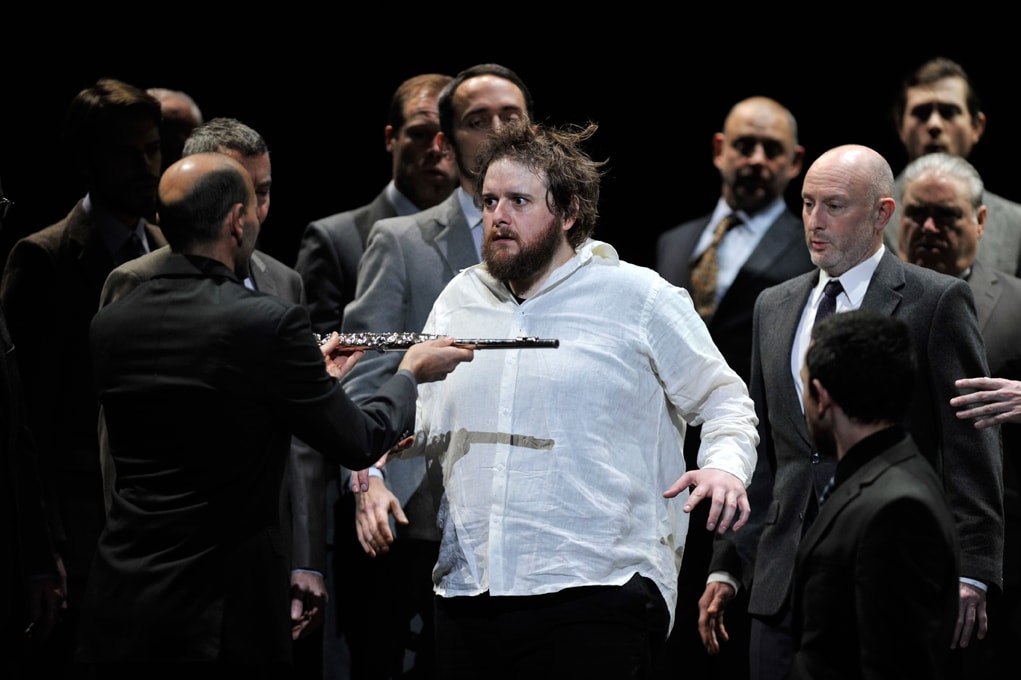 Bearded man in white shirt being presented with a flute in ENO's The Magic Flute