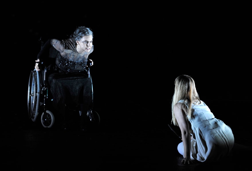 Elderly woman in a wheelchair looking down at a young woman in ENO's The Magic Flute