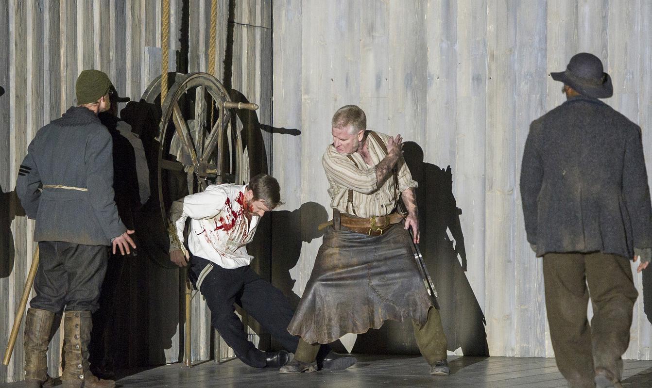 Man being tortured while tied to a large wheel in ENO's Norma