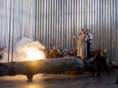 norma marjorie owens and peter auty walking on a log with fire onstage with eno chorus