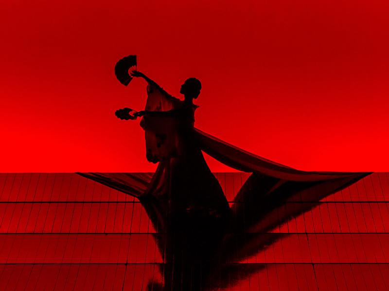 Silhouette of Madam Butterfly holding a hand fan in each hand in front of red lit background
