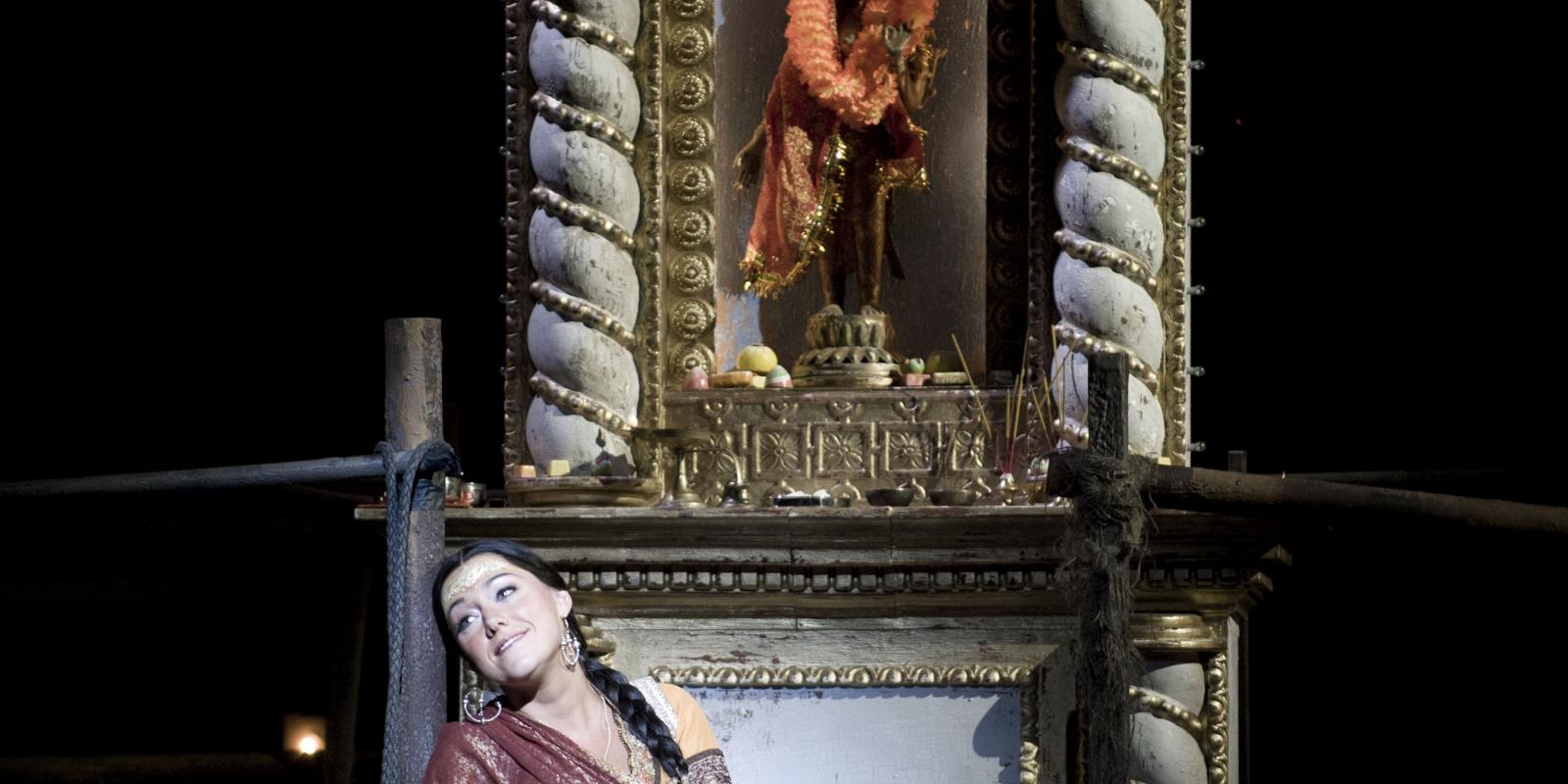 Woman in red dress look off into audience in ENO's The Pearl Fisher