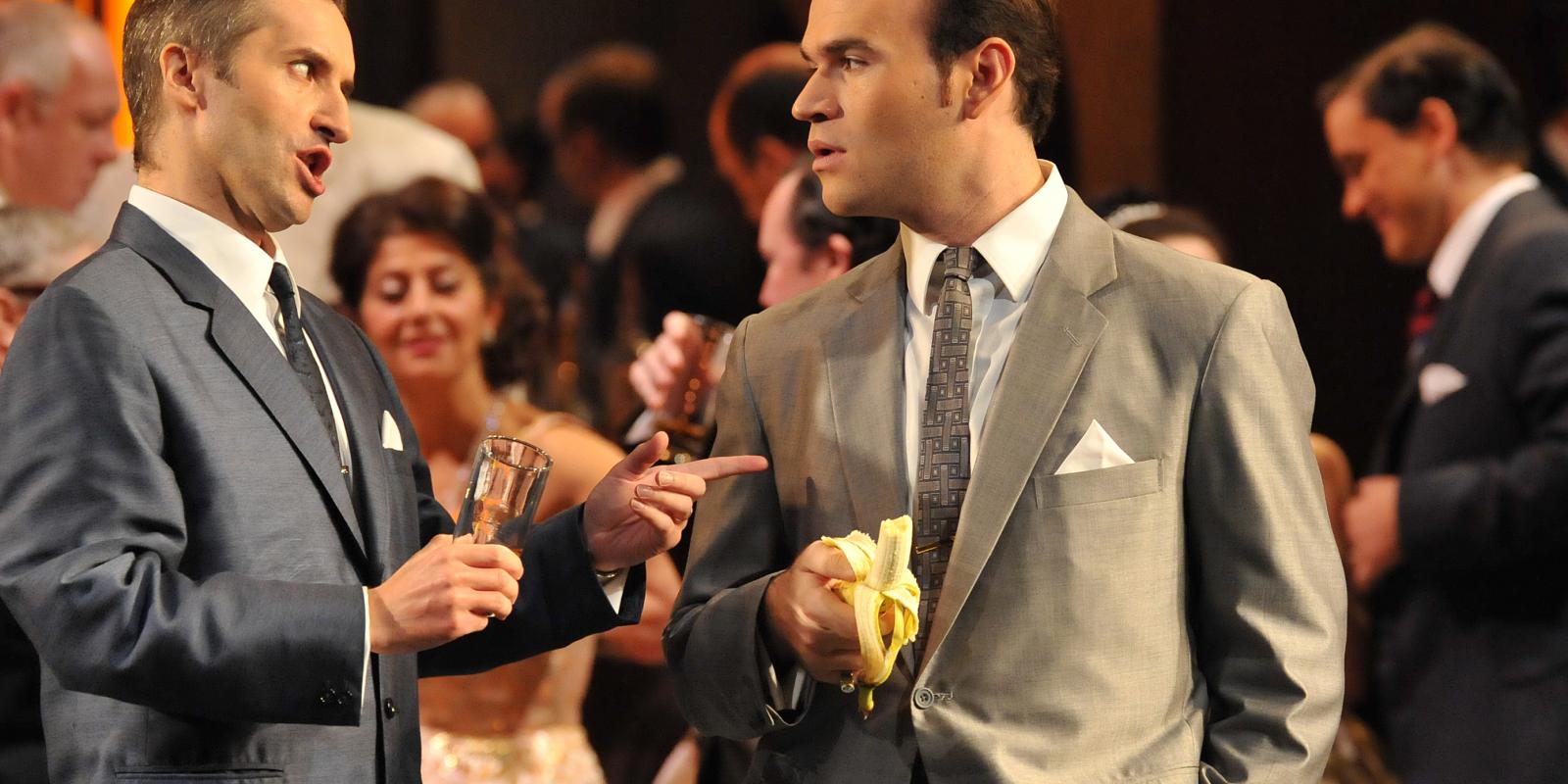 one man drinking and another eating a banana as part of ENO's Rigoletto