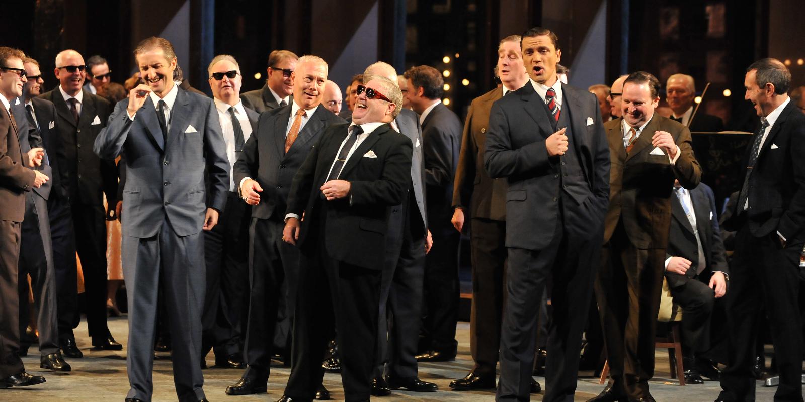 male chorus from rigoletto performing on stage in suits