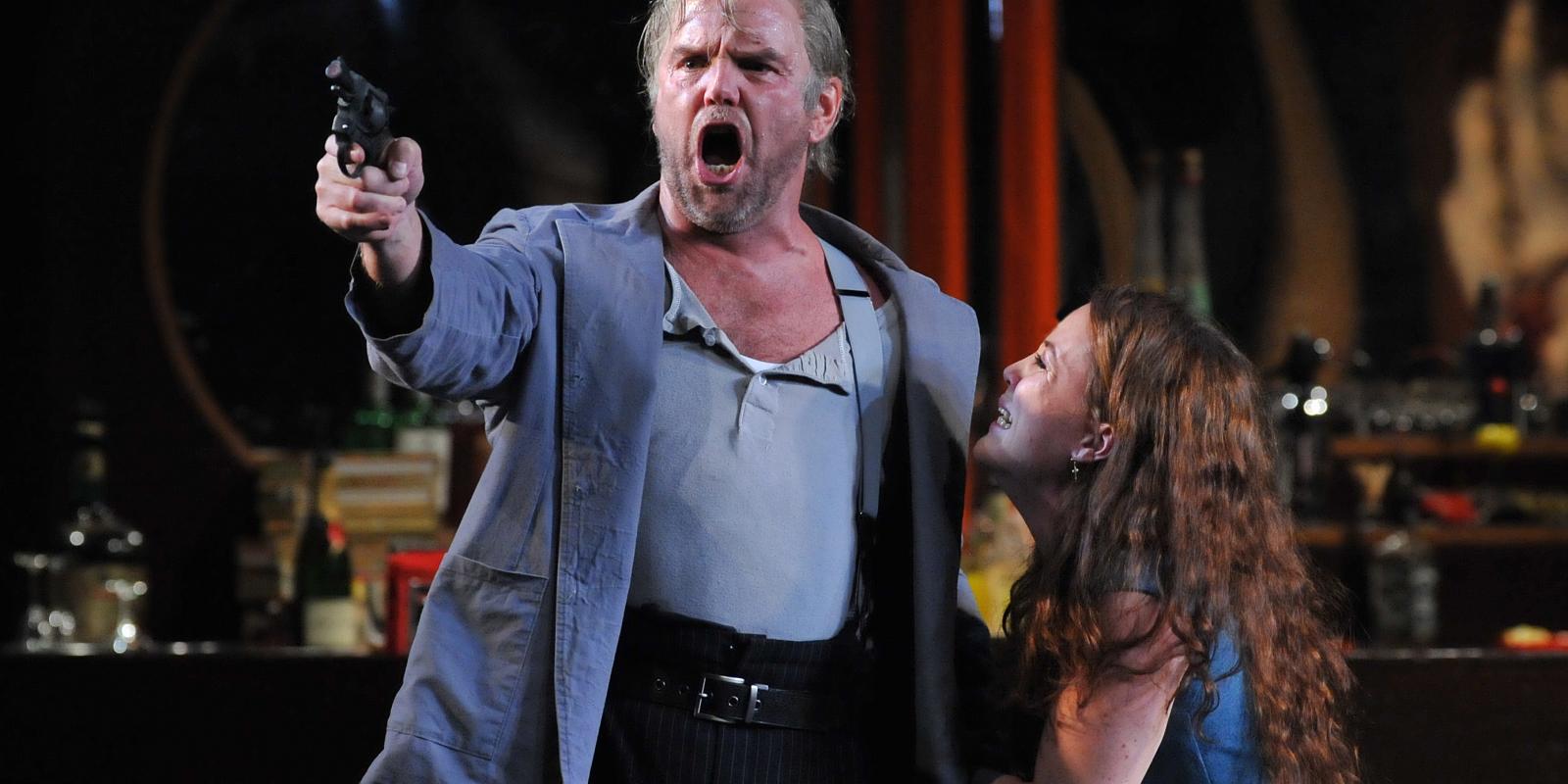 anthony michaels moore holding a gun with katherine whyte performing on stage in Rigoletto