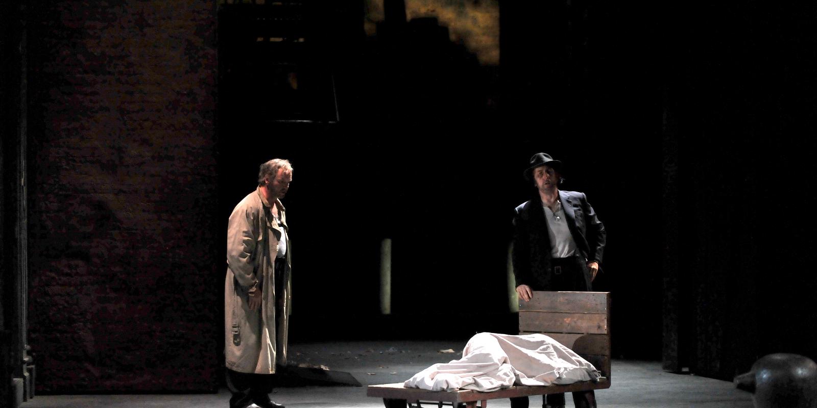 two men sing on stage over body covered with white sheet in Rigoletto