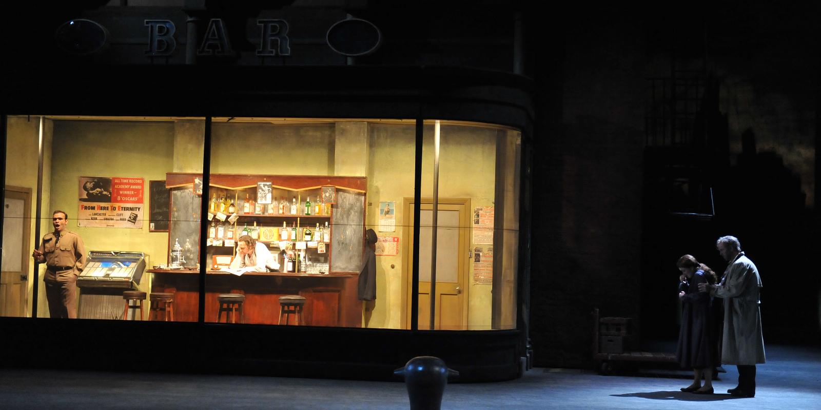 characters stood in and outside of a bar on stage in rigoletto
