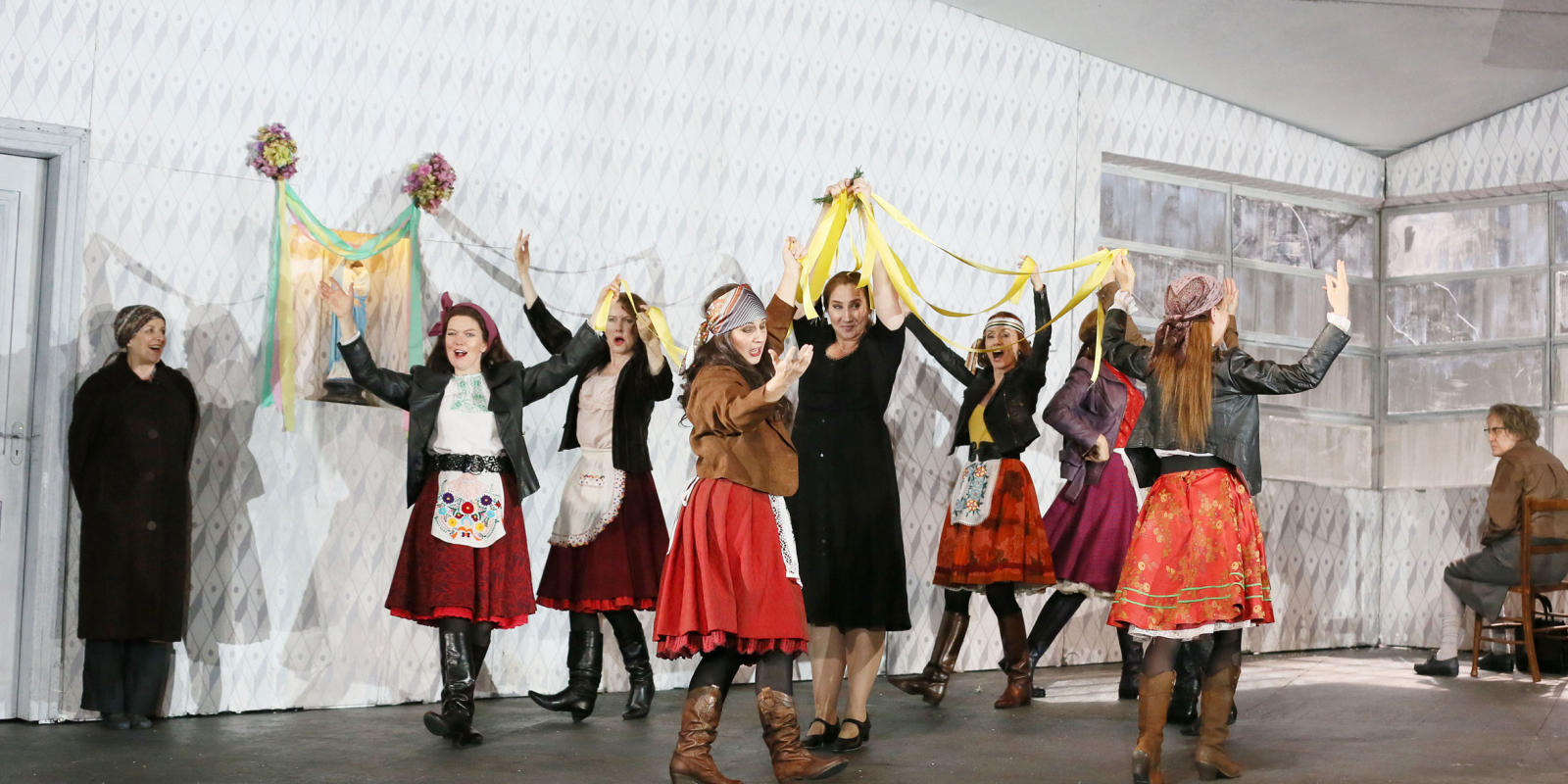 Group of women singing and dancing while holding yellow ribbon in ENO's Jenufa