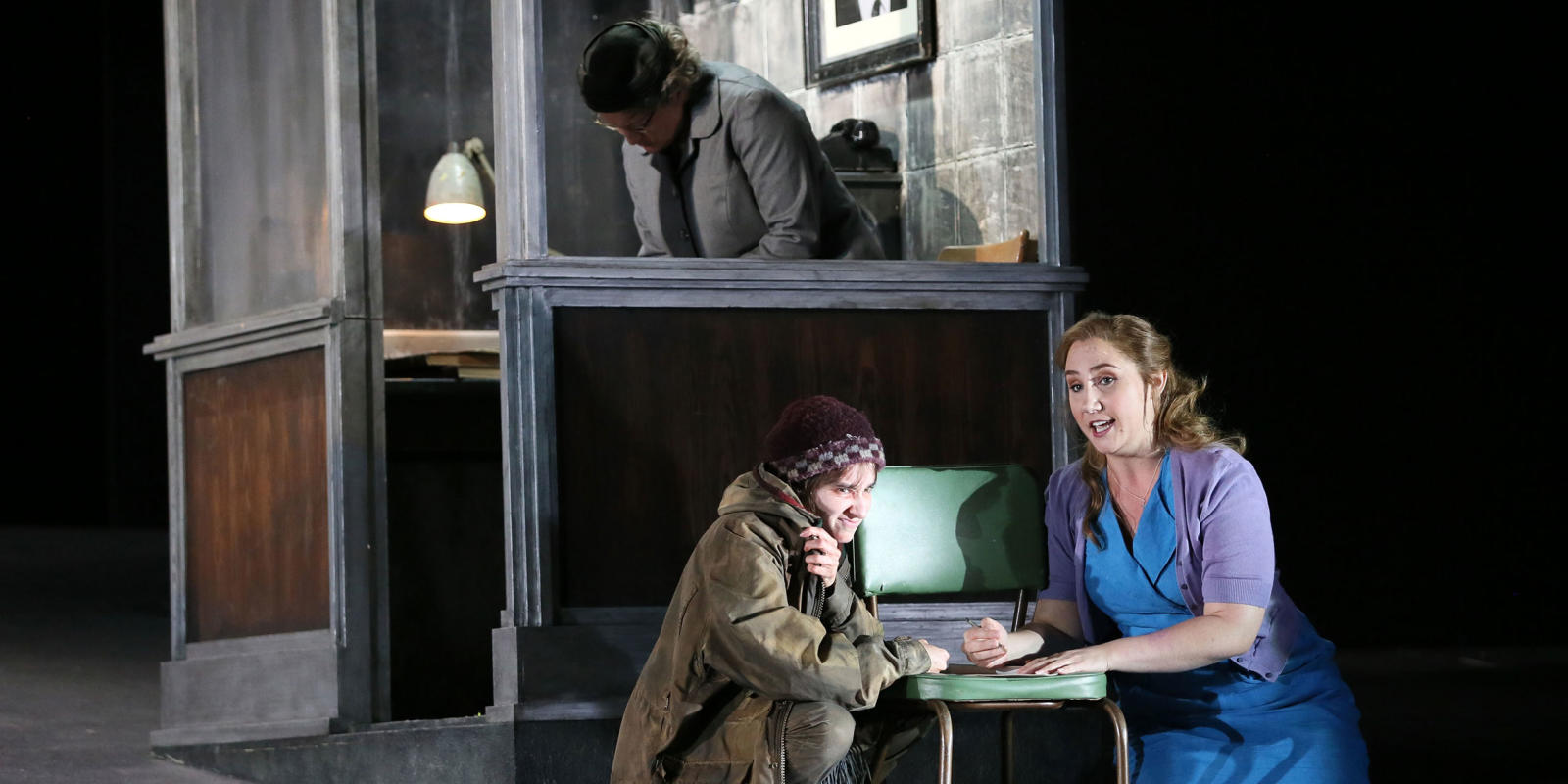 Woman in a blue dress and cardigan sitting with a homeless woman in ENO's Jenufa