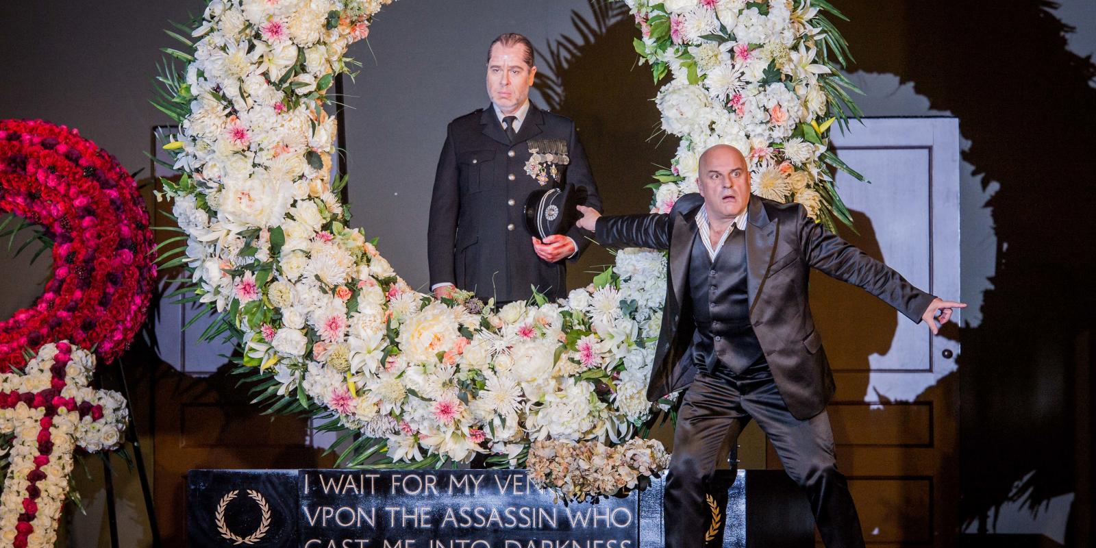 Two men standing around a flower arrangement in ENO's Don Giovanni