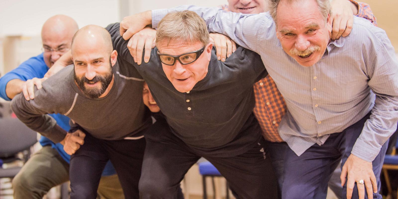 group of men huddled over smiling in Don Giovanni rehearsals