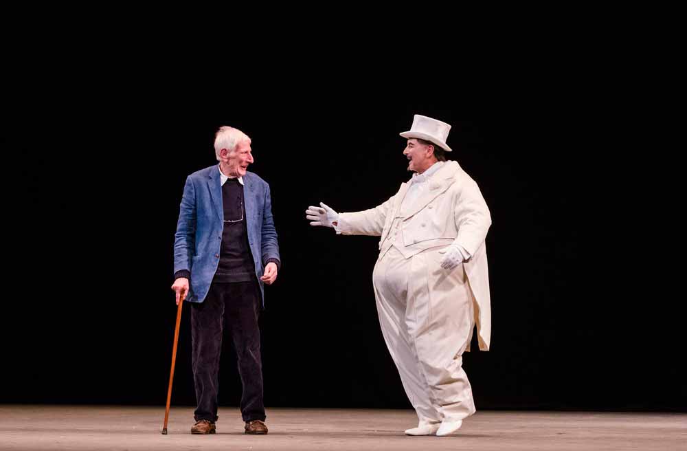 a man in a white suit and top hat, with an elderly gentlemen holding a walking stick