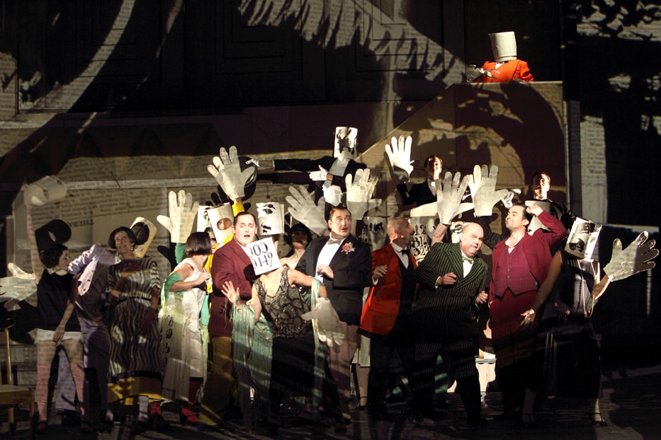 actors on stage suits holding up big paper hands in ENO's Lulu