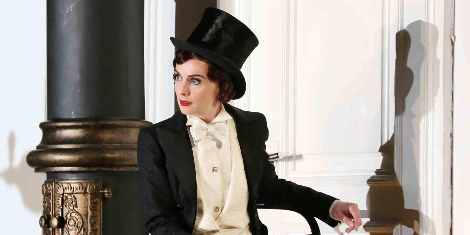 a women sat on a chair in a full suit and top hat