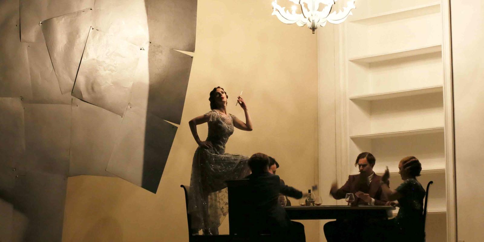a women standing on a chair, four people sat around a table below her