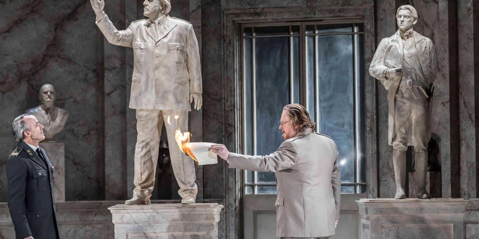 Man in room full of statues holding a burning piece of paper in ENO's The Winter's Tale