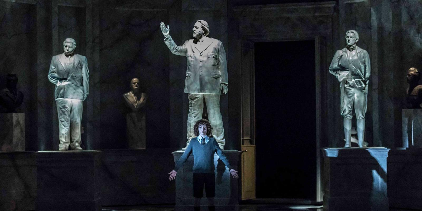 Young boy with curly hair standing in front of 3 statues in ENO's The Winter's Tale