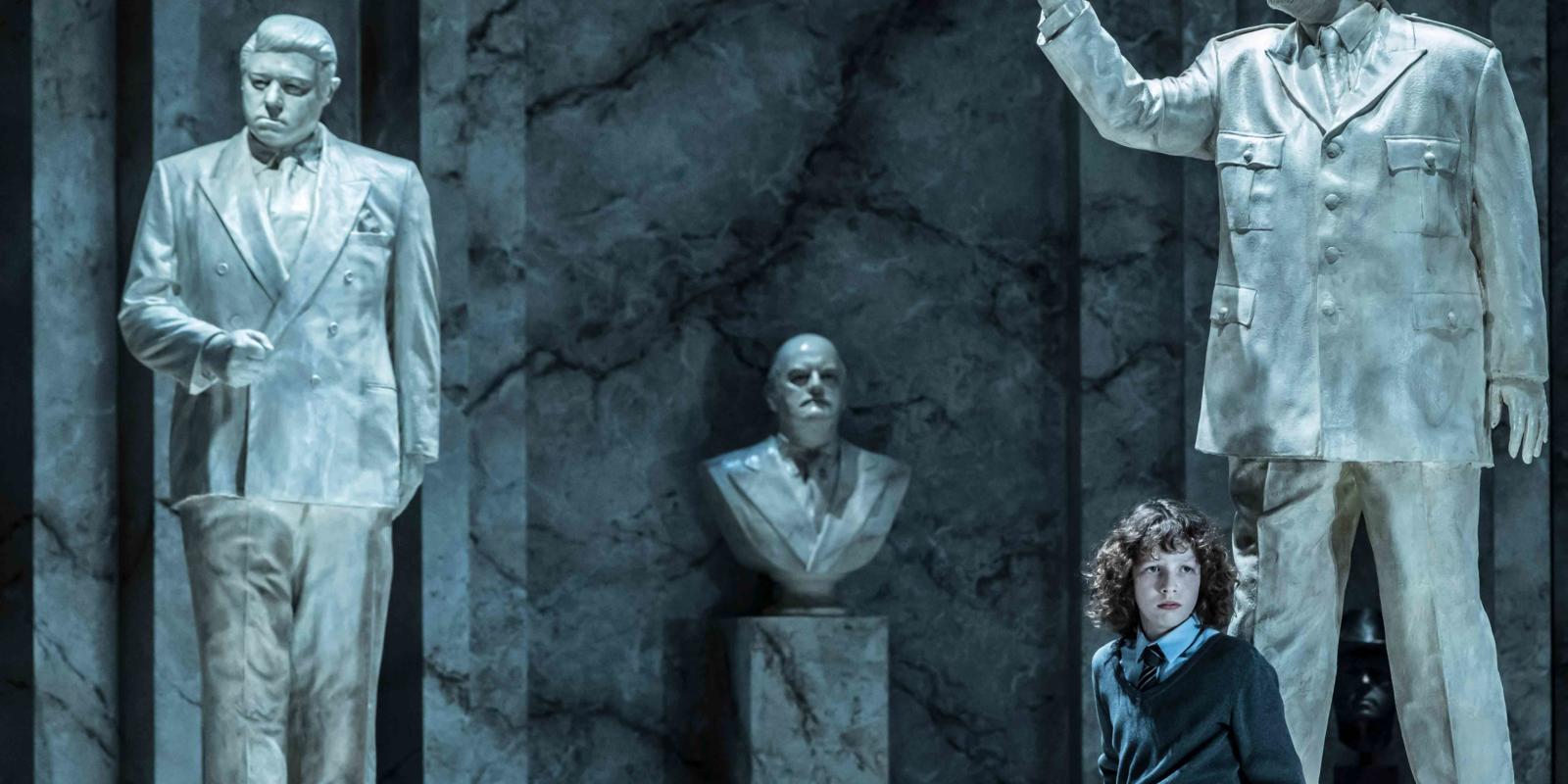young boy in front of three male statues in ENO's The Winter's Tale