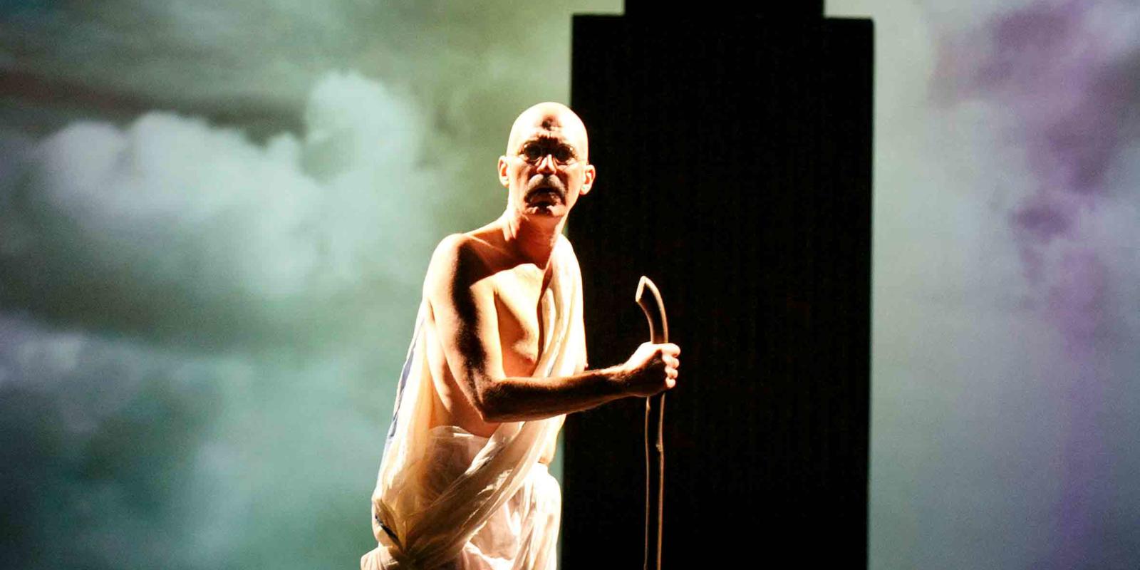 a man in white with a walking stick looking shocked towards the stage. Backdrop looking fiery