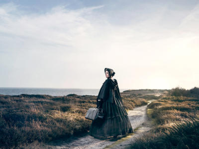 The Governess wearing a bonnet stood on a sandy dune next to the sea