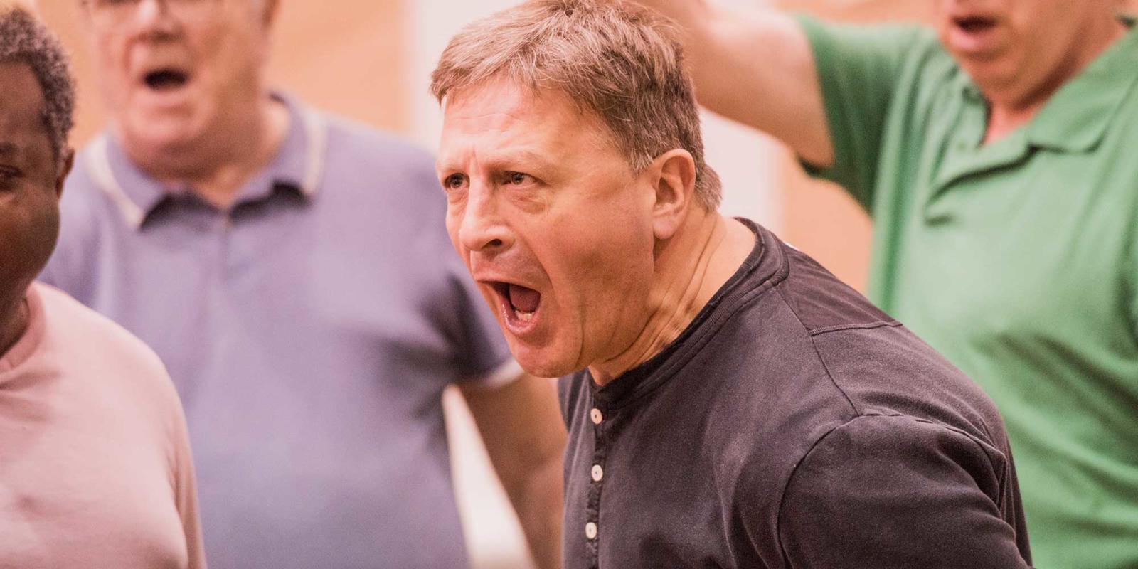 Man in a dark shirt singing during rehearsals for ENO's Don Giovanni