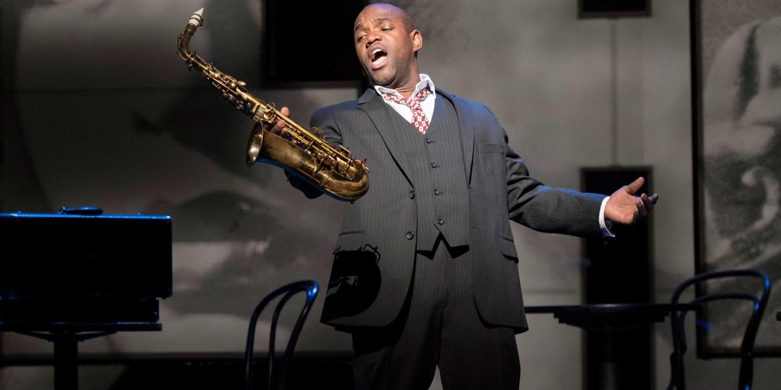 a man holding up his saxophone singing