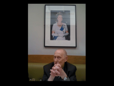 tony browne sat in front of framed photo of the queen