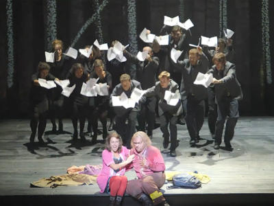 two people at the front of the stage with the ENO chorus behind