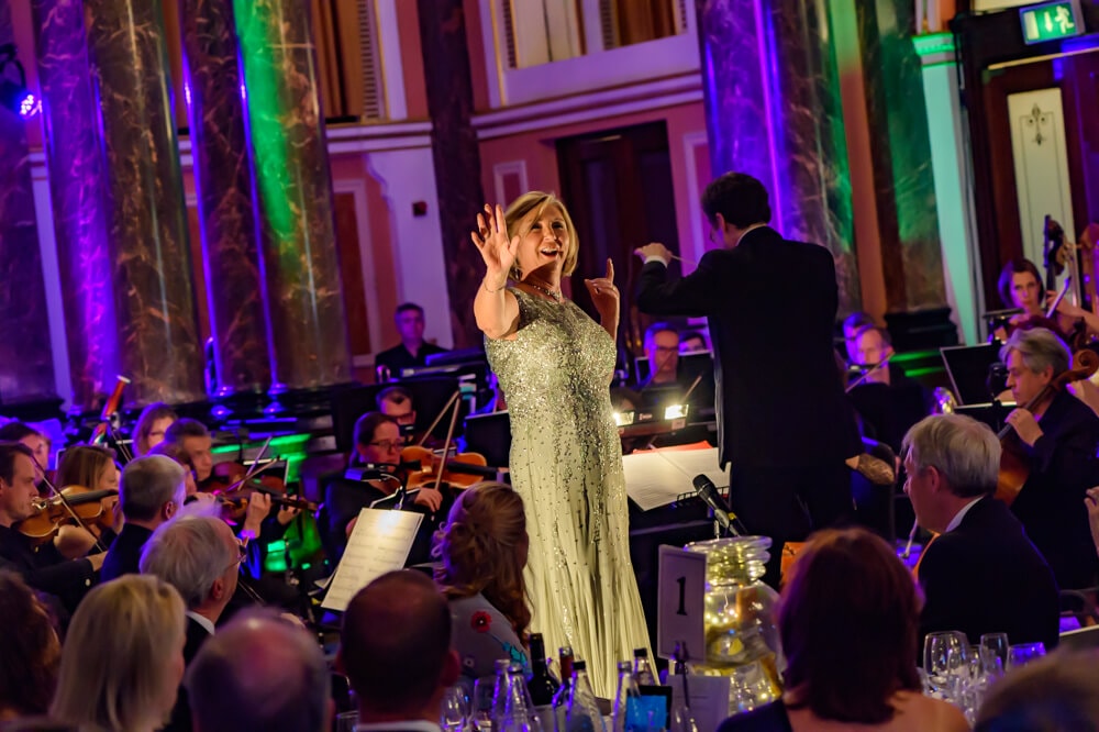 Woman in silver dress singing at ENO's Gala Dinner