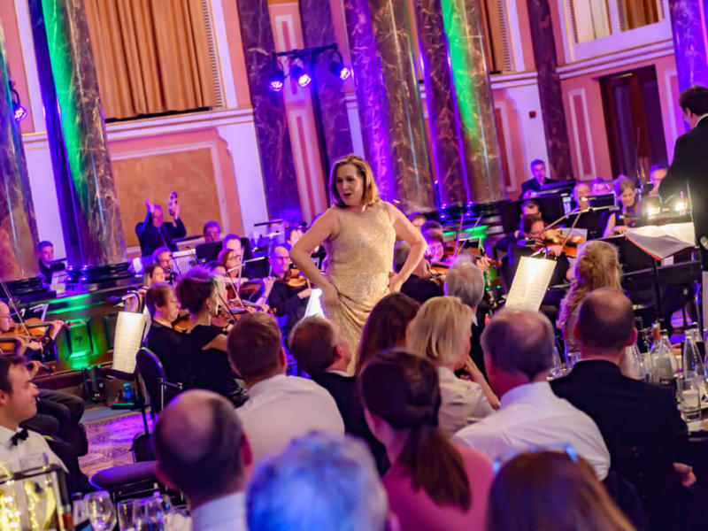 Woman singing to guests in front of an orchestra at ENO's Gala Dinner