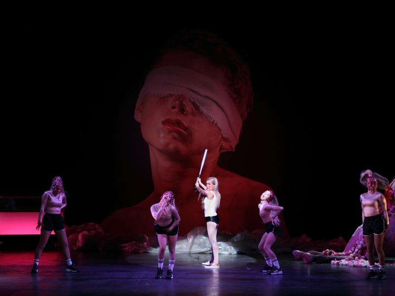 Salome title role posed with a baseball bat surrounded by dancers wearing sporting gear and sparkly headbands