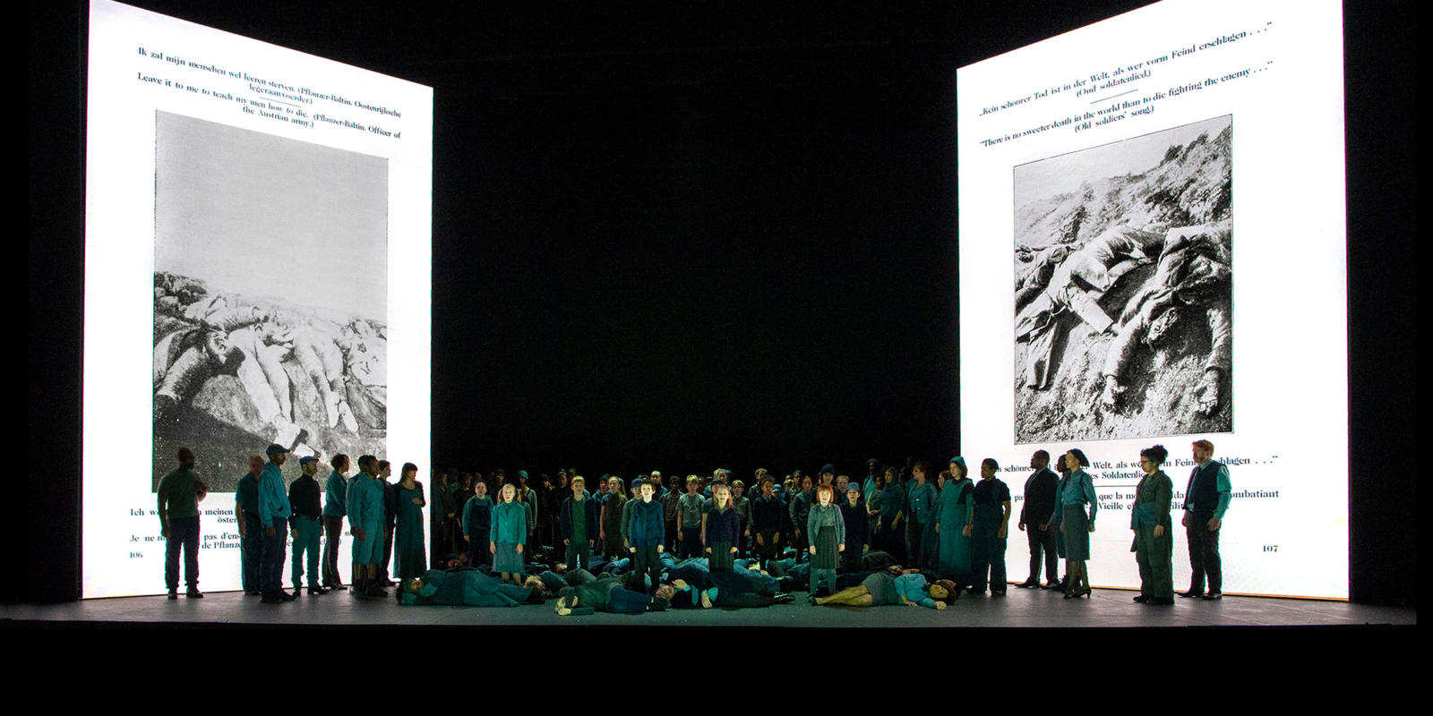 Ensemble of War Requiem stood on stage with projections of a German anti-war pamphlet behind them