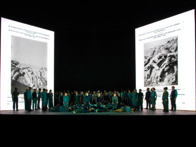 Ensemble of War Requiem stood on stage with projections of a German anti-war pamphlet behind them