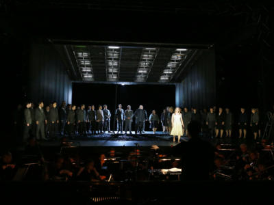 Cast members of The Magic Flute stood on a dimly lit stage with the orchestra playing in front