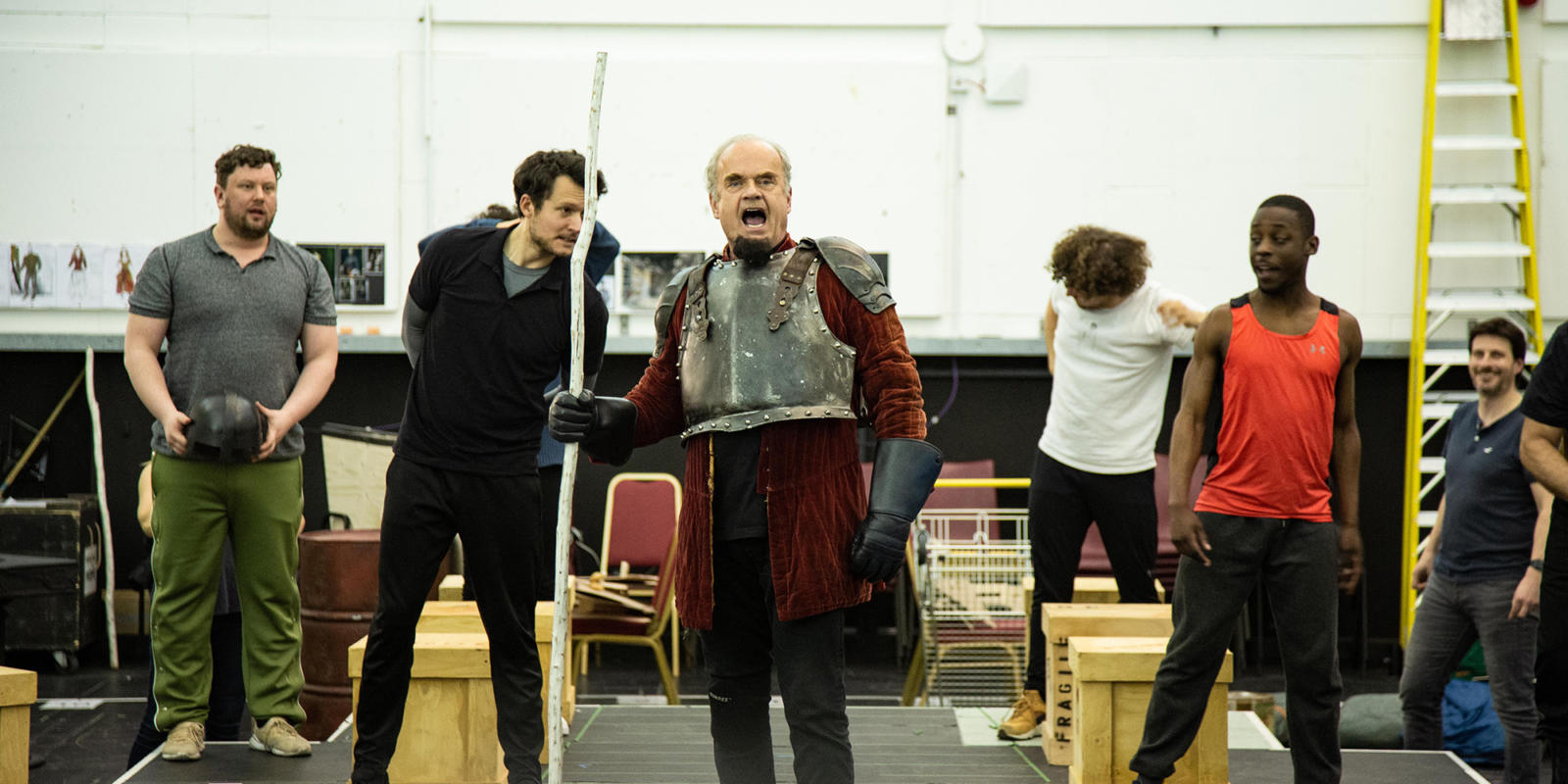 Kelsey Grammer in armour and with a stick in rehearsal with other actors