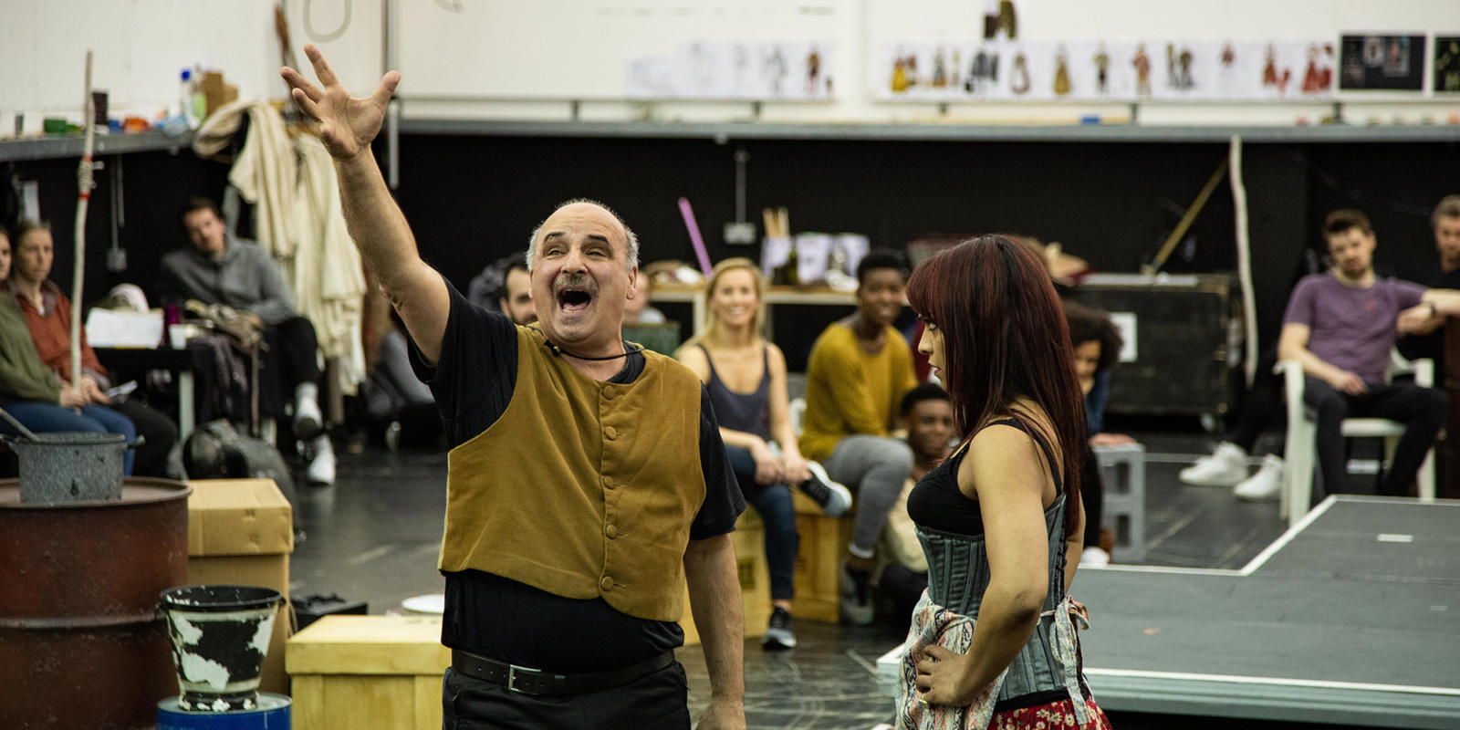 Peter Polycarpou performing with his arm raised with Danielle de Niese and other actors