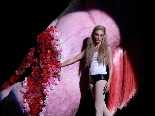 Alison Cooke as Salome wearing black leather underwear stood with her hand inside a giant decapitated pink pony with flowers in place of blood