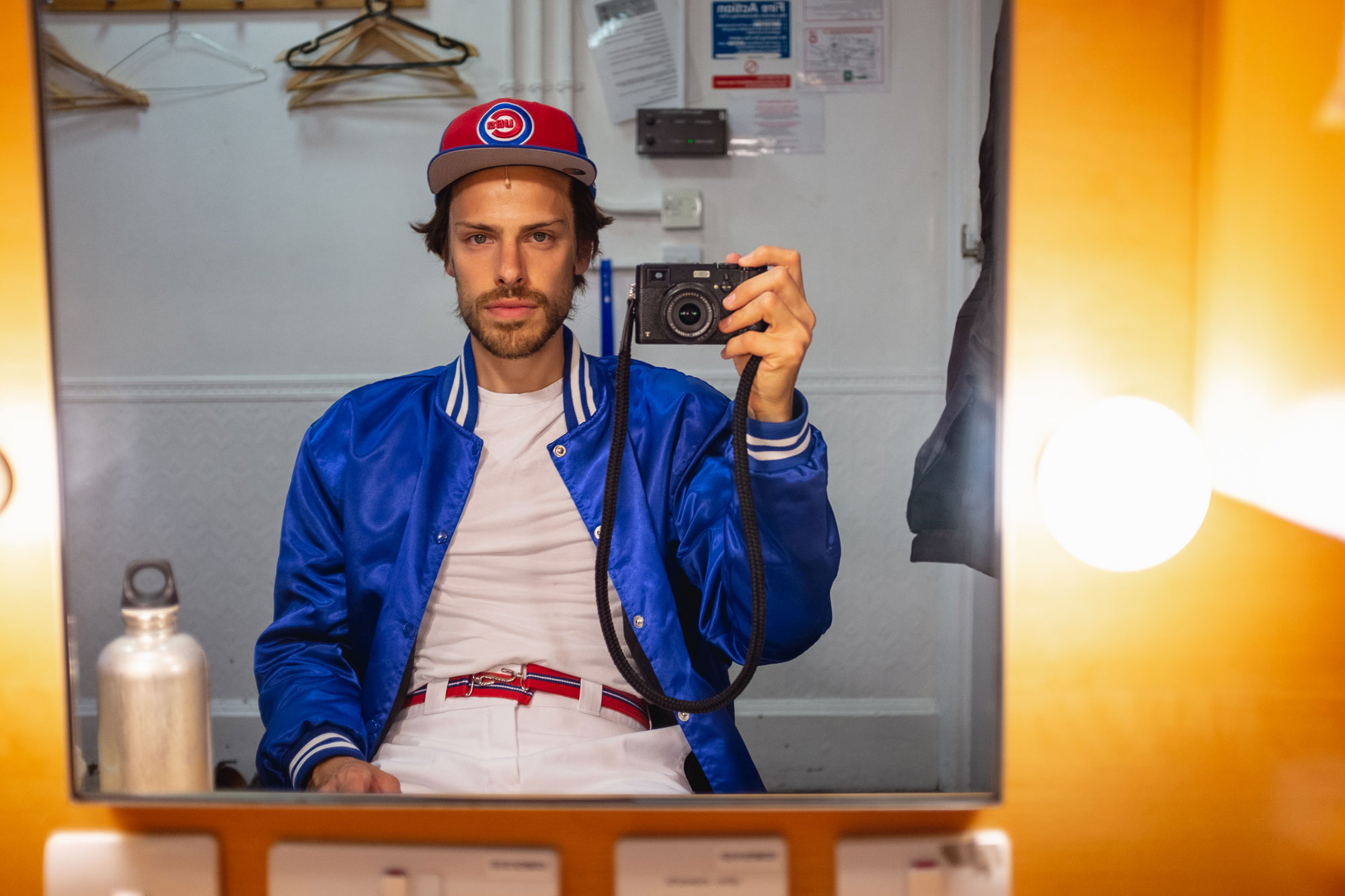 man taking a picture in the mirror: wearing a baseball hat and jacket