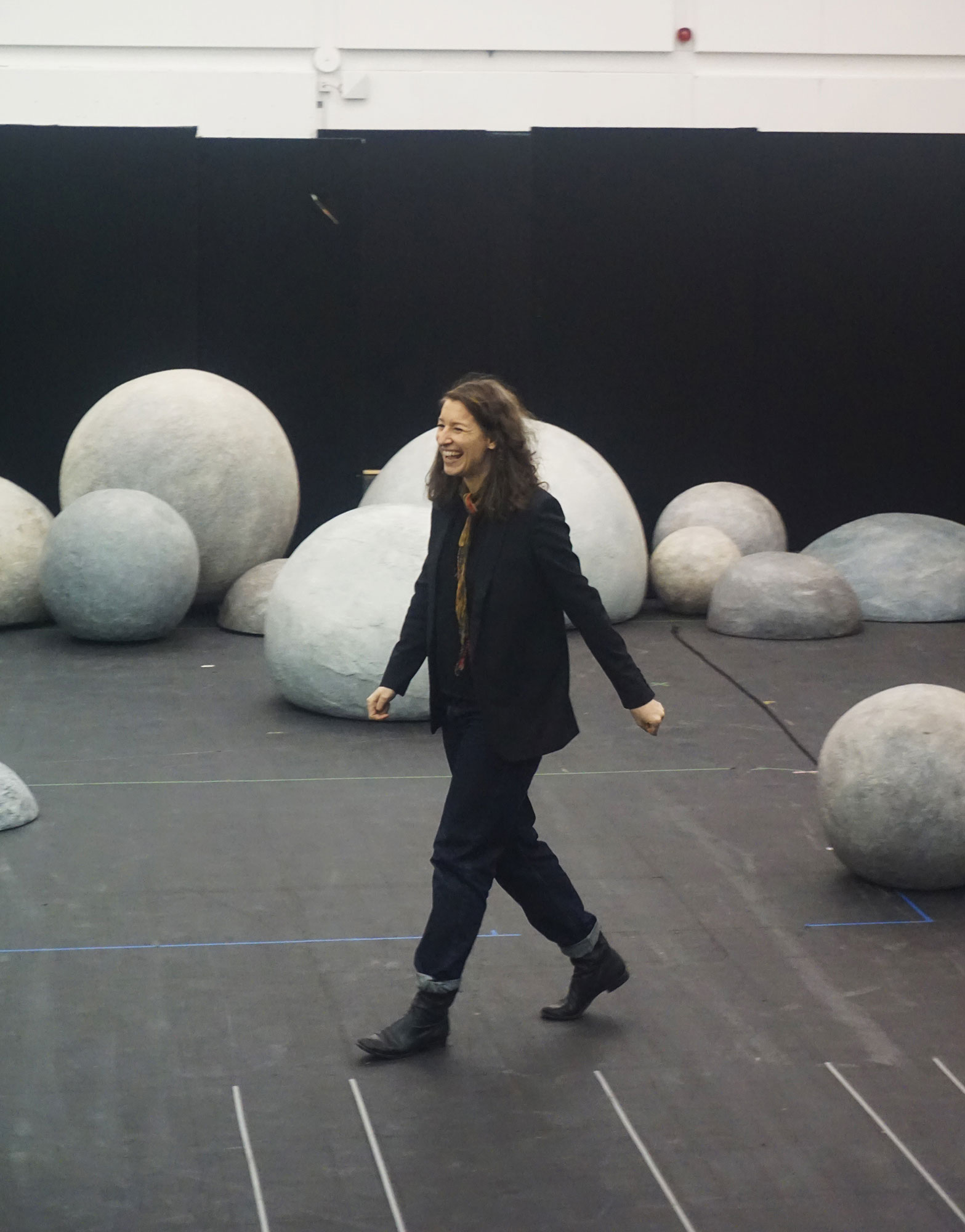 woman smiling whilst walking past grey spherical shaped props