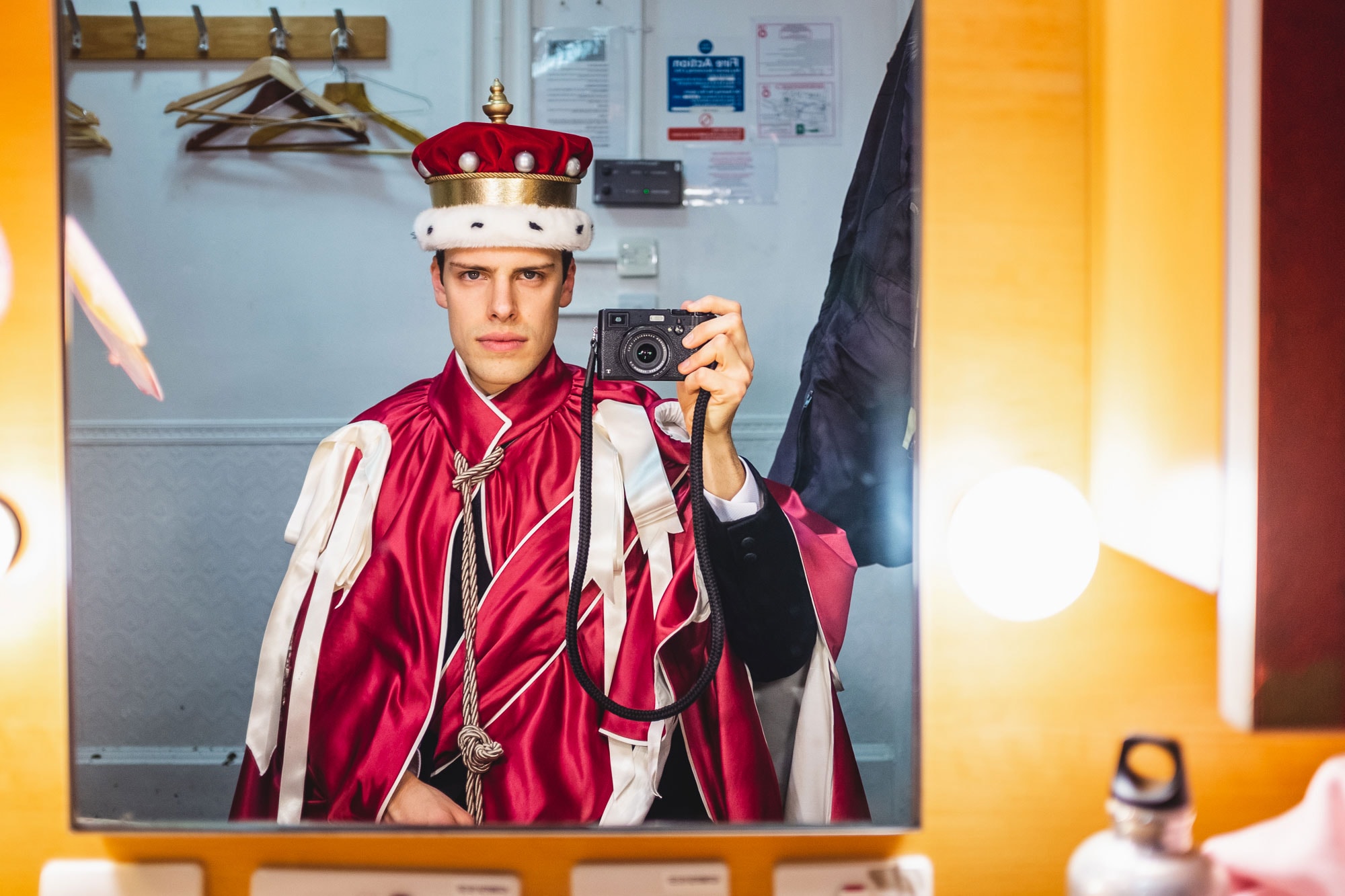 man taking a picture in the mirror: wearing a royal robe and crown