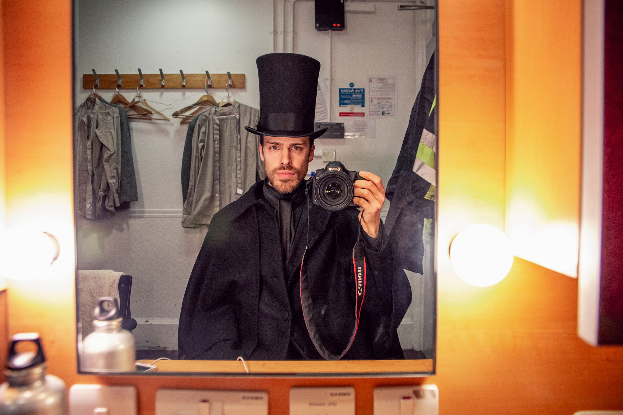 man taking a picture in the mirror: wearing a full suit and top hat