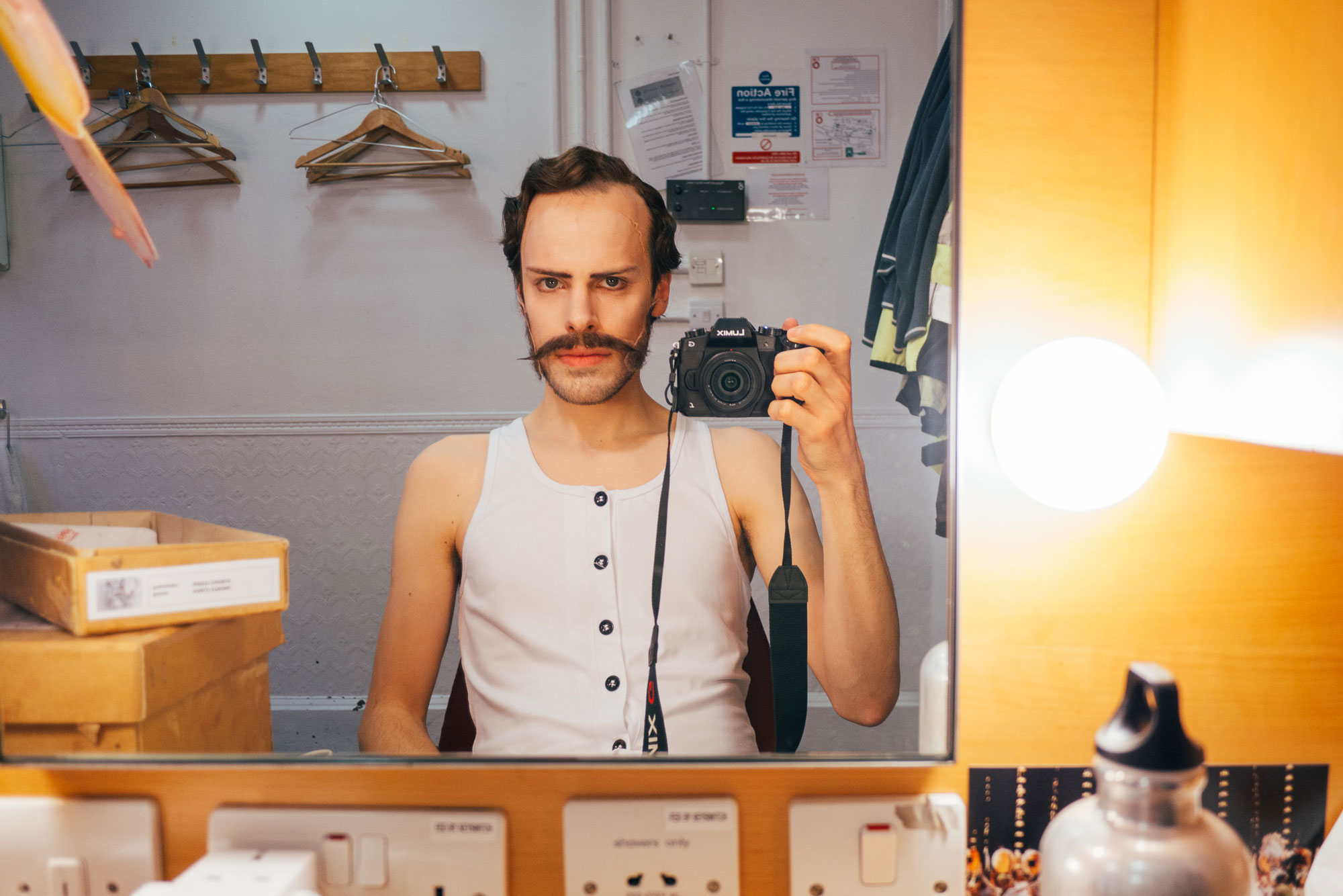man taking a picture in the mirror: wearing a fake mustache and vest