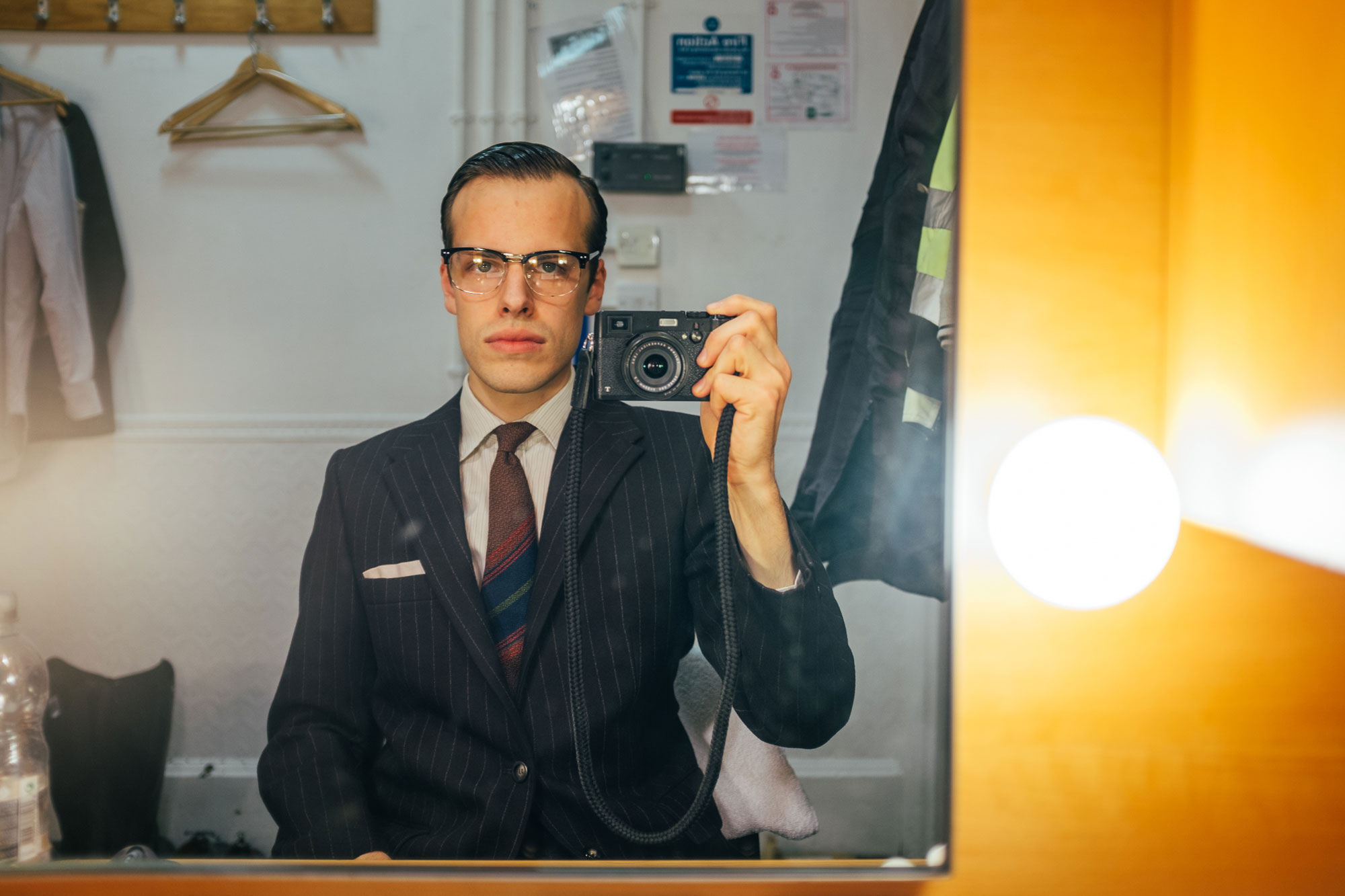 man taking a picture in the mirror: wearing a striped suit and glasses