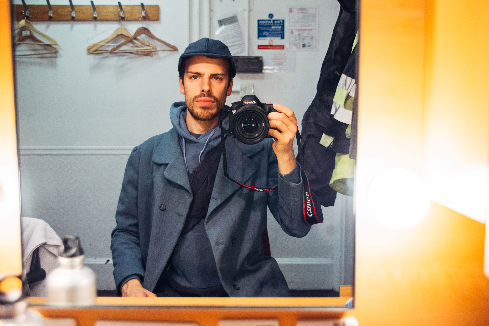 man taking a picture in the mirror: wearing a hoodie and cap