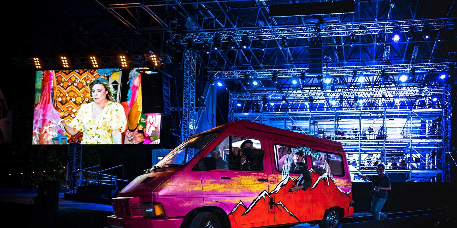 A van on stage, with Mimi shown on a giant screen.