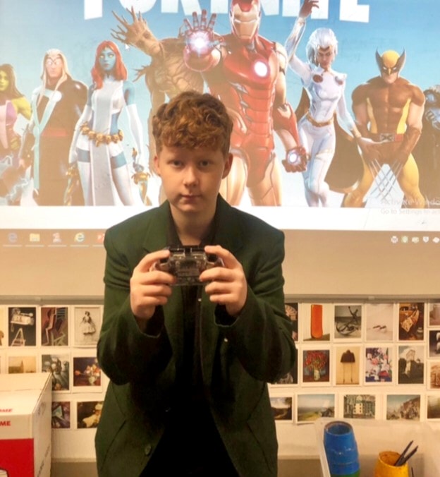 School boy holding camera up in front of a marvel poster