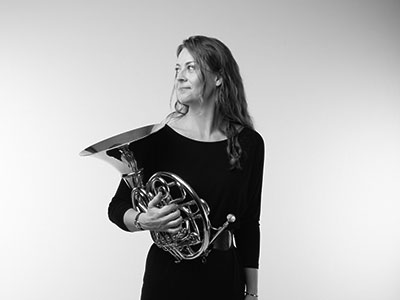 Corinne Bailey holding a french horn and looking away from camera