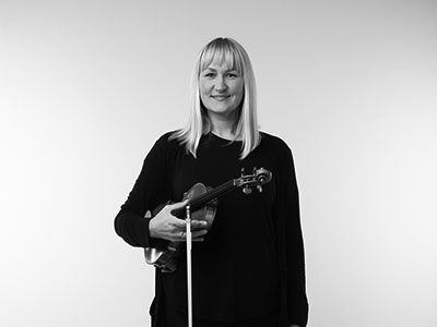 Cath Haggo holding a violin and smiling to camera